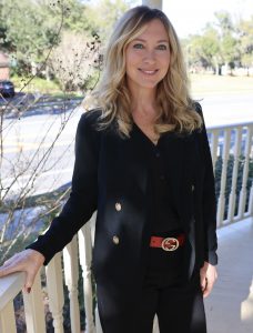 a portrait of the teacher, who is standing outside on a porch with her hand on a porch railing